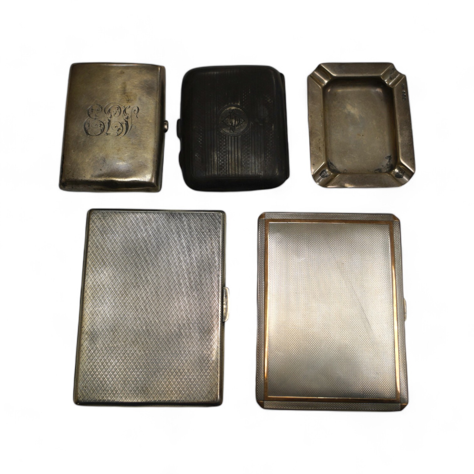 A George VI engine turned silver cigarette case, with yellow metal band, London, 1938, 11.4cm, four other silver cigarette cases and a silver ashtray, gross weight 16.8oz. Condition - poor to fair